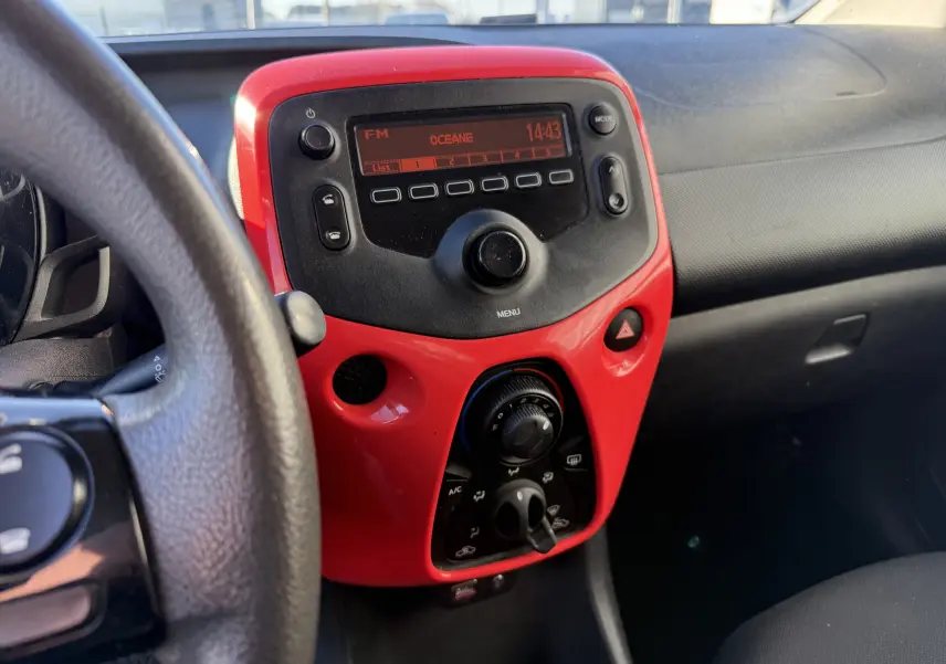 Tableau de bord intérieur d'une Citroën C1 2014, avec console centrale rouge et commandes radio et climatisation visibles.