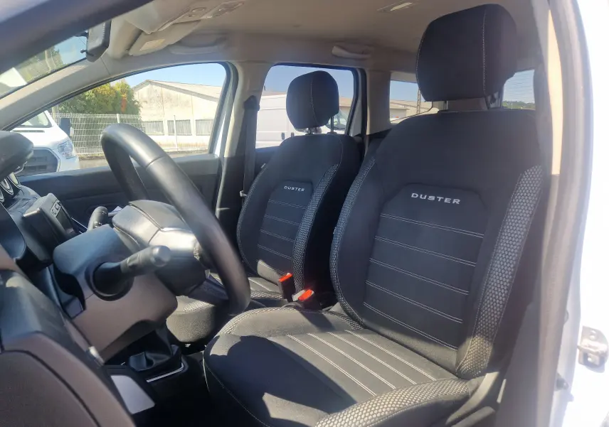 Vue intérieure côté conducteur du Dacia Duster blanc 2021, sièges noirs avec logo Duster brodé.