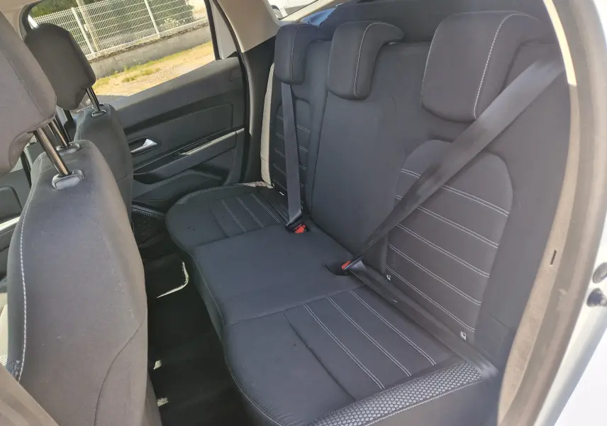 Vue intérieure côté droit des sièges arrière noirs du Dacia Duster 2021 blanc, avec ceintures de sécurité attachées.