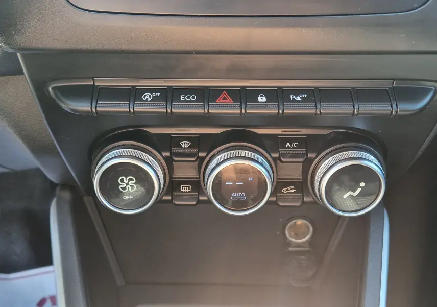 Vue rapprochée des commandes de climatisation et des boutons de fonction du tableau de bord du Dacia Duster blanc 2021.