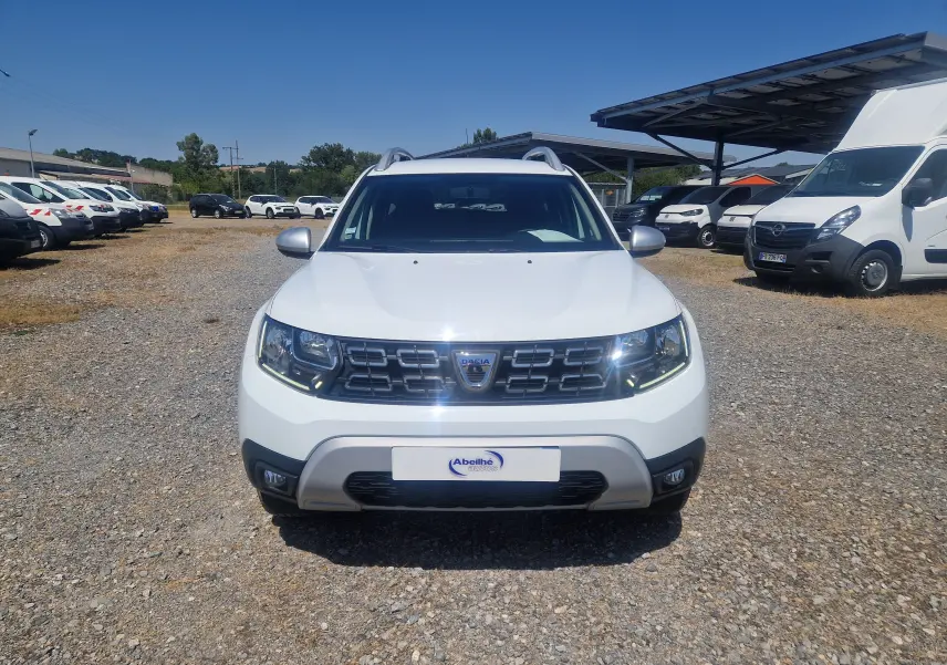 Vue de face du Dacia Duster blanc 2021, mettant en valeur sa calandre distinctive et ses phares LED allumés.