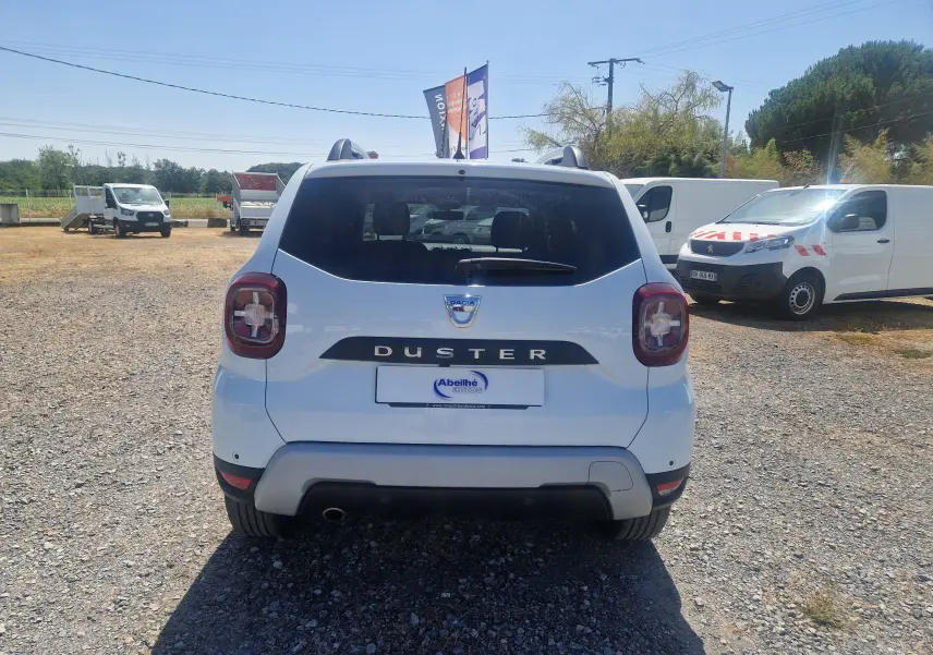 Vue arrière d'un Dacia Duster blanc 2021, avec feux arrière distinctifs et logo bien visible sur un terrain extérieur.