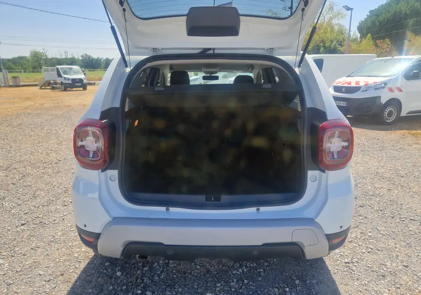 Vue arrière ouverte du Dacia Duster blanc 2021, coffre spacieux visible avec hayon relevé en extérieur.