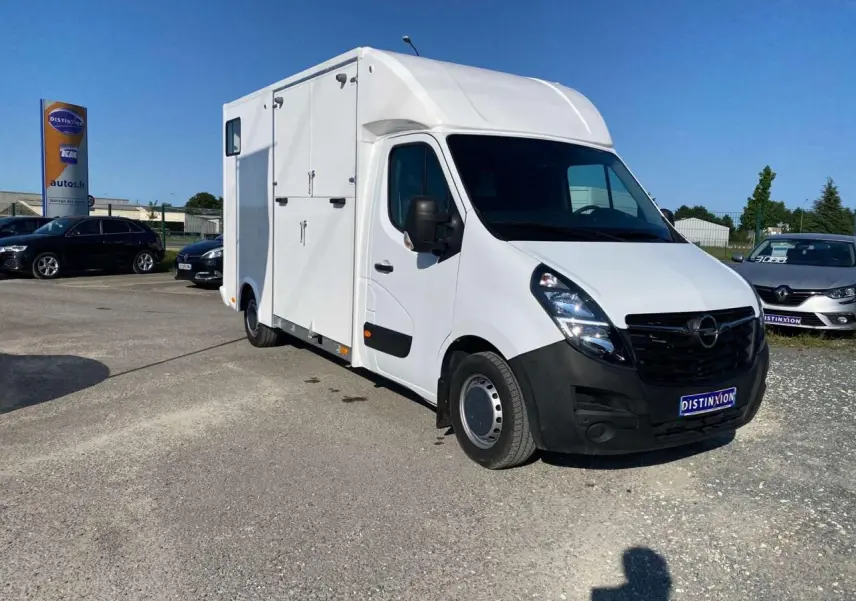 Vue 3/4 avant droit d'un Opel Movano Fourgon blanc avec capucine et portes latérales sur parking.