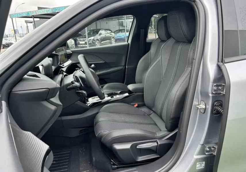 Vue intérieure côté conducteur du Peugeot 2008 gris Artense, sièges tissu et cuir avec surpiqûres vertes et volant compact cuir.