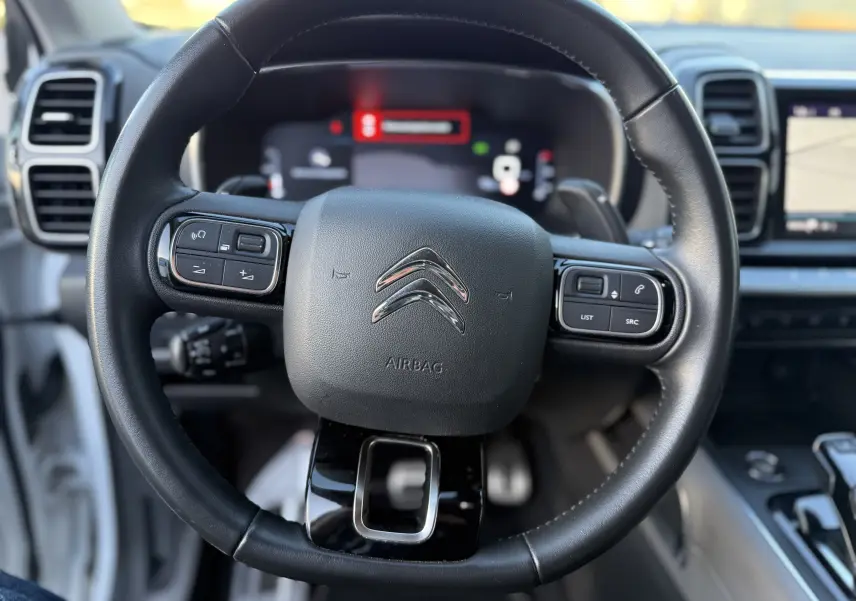Vue rapprochée du volant cuir noir du Citroën C5 Aircross 2021, avec commandes intégrées et tableau de bord numérique flou.