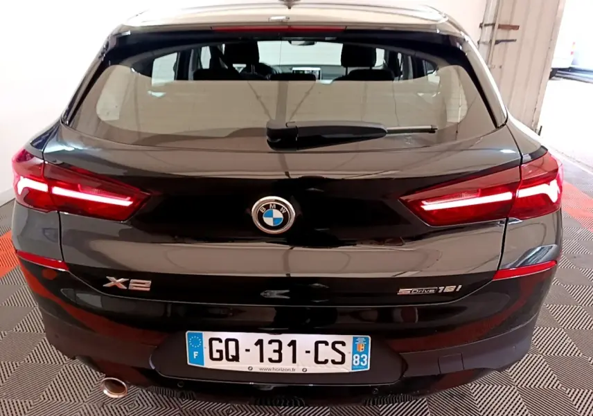 Vue arrière d'une BMW X2 sDrive18i Lounge noire avec feux LED allumés et plaque d'immatriculation française visible.