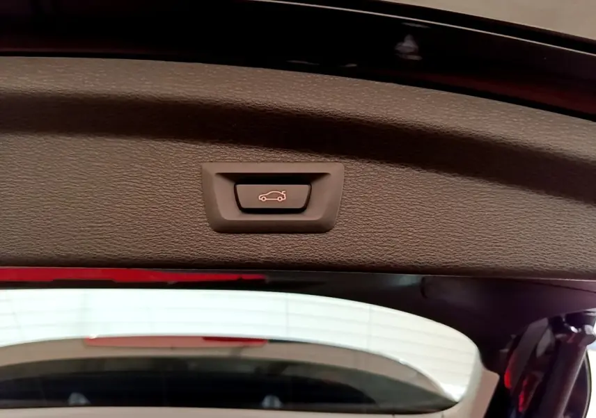 Bouton d'ouverture électrique du coffre sur la partie intérieure du hayon d'une BMW X2 noire vue de l'arrière.