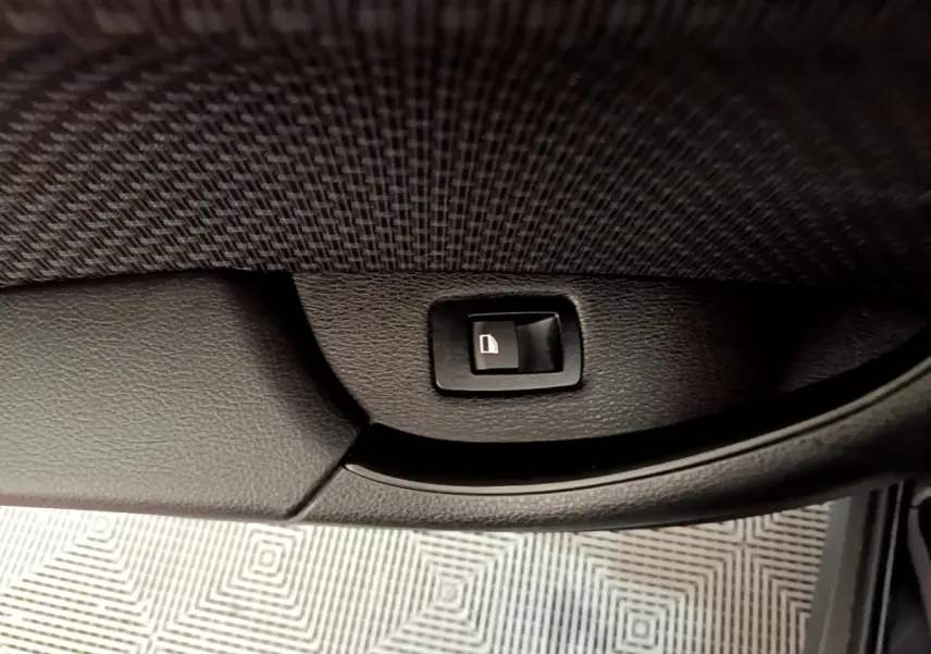 Gros plan sur le bouton de verrouillage de porte noir à l'intérieur de la portière côté conducteur d'une BMW X2 noire.