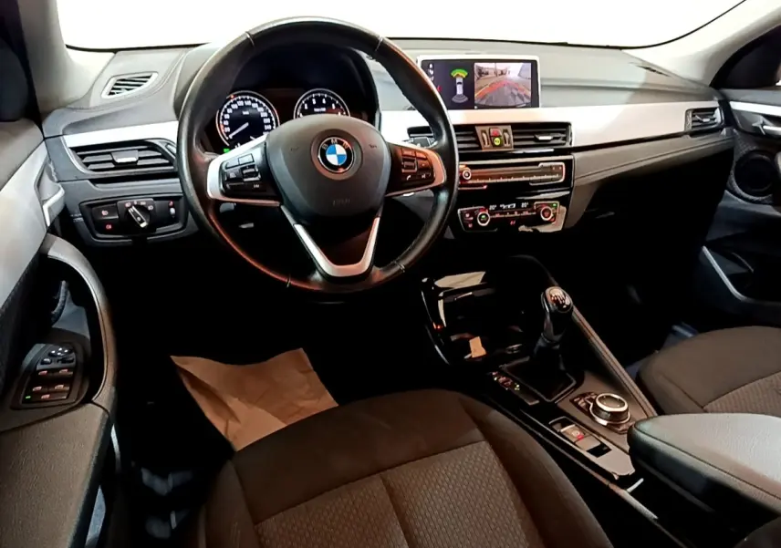 Intérieur BMW X2 sDrive18i 2023 vu de face, volant cuir, tableau de bord avec écran multimédia et levier de vitesse manuel.