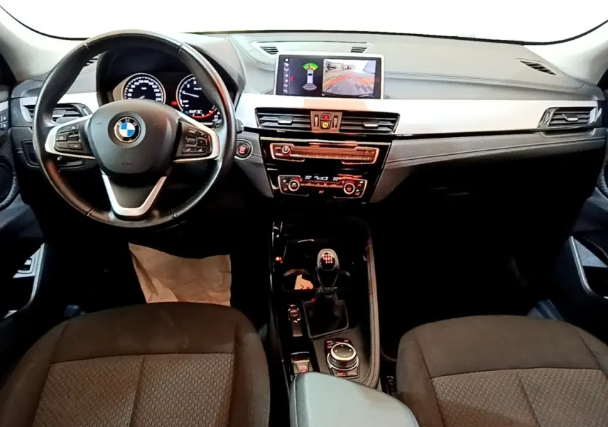 Vue intérieure avant du BMW X2 sDrive18i Lounge 2023 noir, volant cuir, écran central avec affichage caméra de recul.