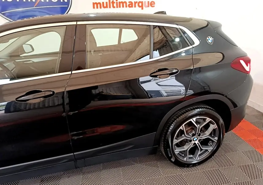 Vue latérale droite du BMW X2 sDrive18i Lounge noir, mettant en valeur la jante alliage et le logo BMW arrière.