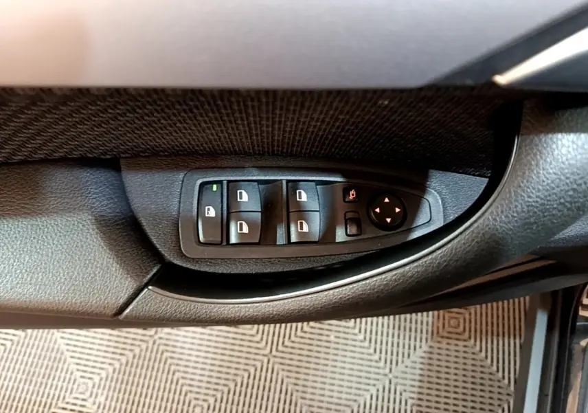 Vue rapprochée des commandes de lève-vitres et rétroviseurs sur la porte côté conducteur d'une BMW X2 noire.