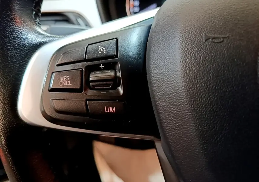 Gros plan sur les commandes du régulateur de vitesse au volant cuir noir d’une BMW X2 sDrive18i Lounge 2023.