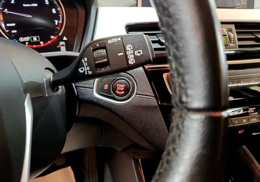 Gros plan sur le volant et le bouton start/stop rouge du tableau de bord noir du BMW X2 sDrive18i Lounge 2023.