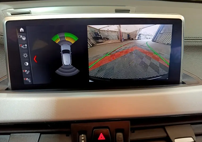 Écran central du BMW X2 sDrive18i 2023 montrant l'aide au stationnement arrière avec caméra et capteurs actifs.