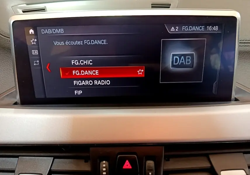 Écran central du tableau de bord du BMW X2 sDrive18i Lounge 2023 affichant la radio DAB en mode FG.DANCE.