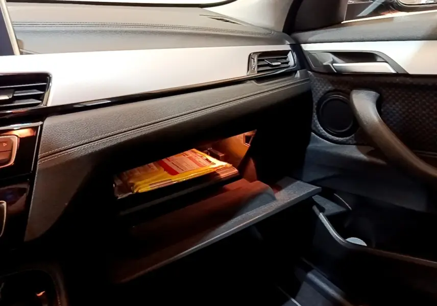 Intérieur BMW X2 sDrive18i 2023 vu côté passager, boîte à gants ouverte avec éclairage intérieur orange.