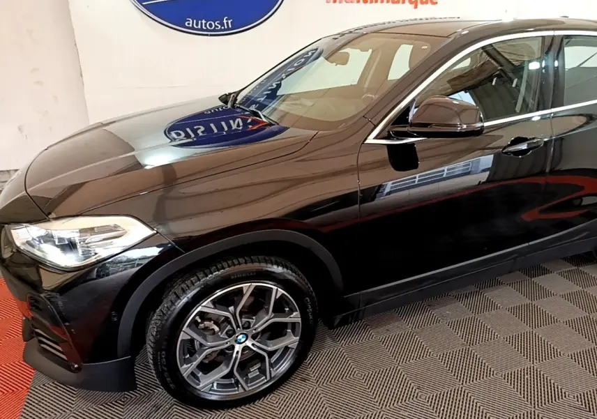 BMW X2 sDrive18i Lounge noir vue 3/4 avant droit, mettant en valeur les jantes alliage et les phares LED distinctifs.