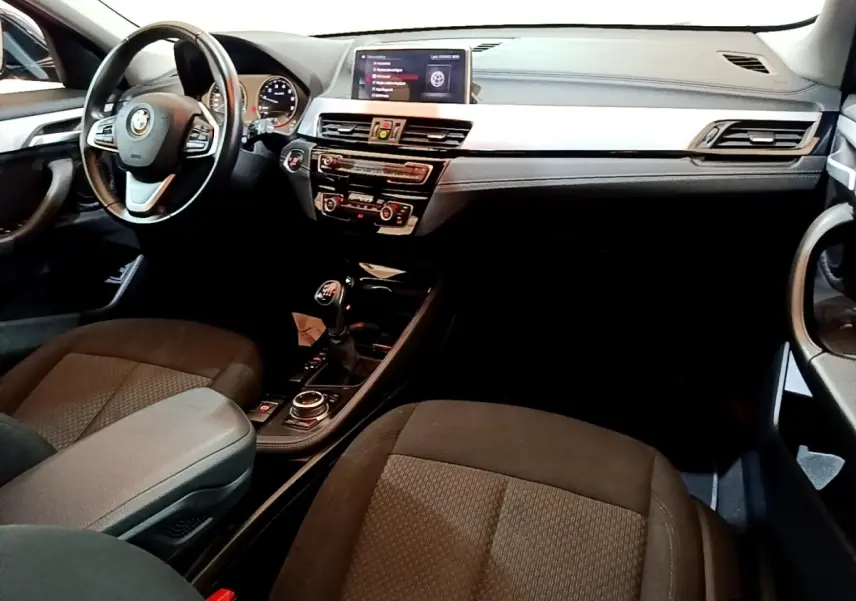Vue intérieure avant droite du BMW X2 sDrive18i Lounge 2023, montrant le tableau de bord et la console centrale avec boîte manuelle.