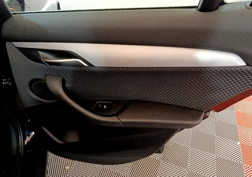 Vue intérieure de la porte arrière gauche noire du BMW X2 sDrive18i Lounge avec habillage tissu et commande de lève-vitre.