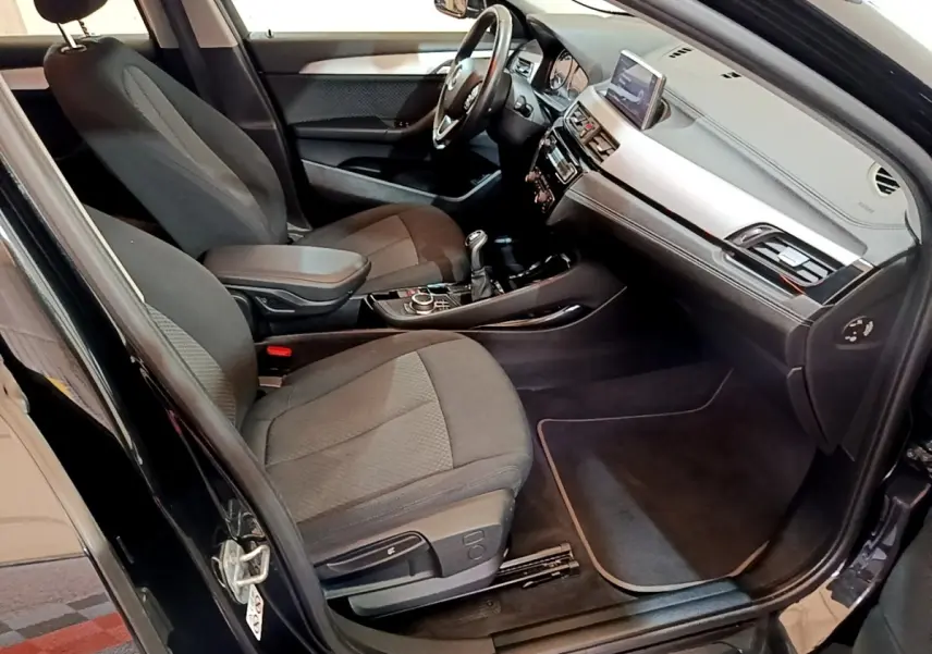 Vue intérieure côté conducteur de la BMW X2 sDrive18i Lounge 2023 noire, avec tableau de bord et console centrale visibles.