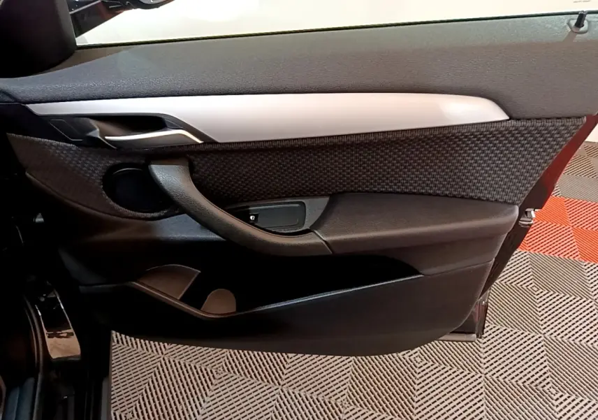 Vue intérieure de la porte avant gauche noire de la BMW X2 sDrive18i Lounge 2023 avec habillage texturé et poignée intégrée.