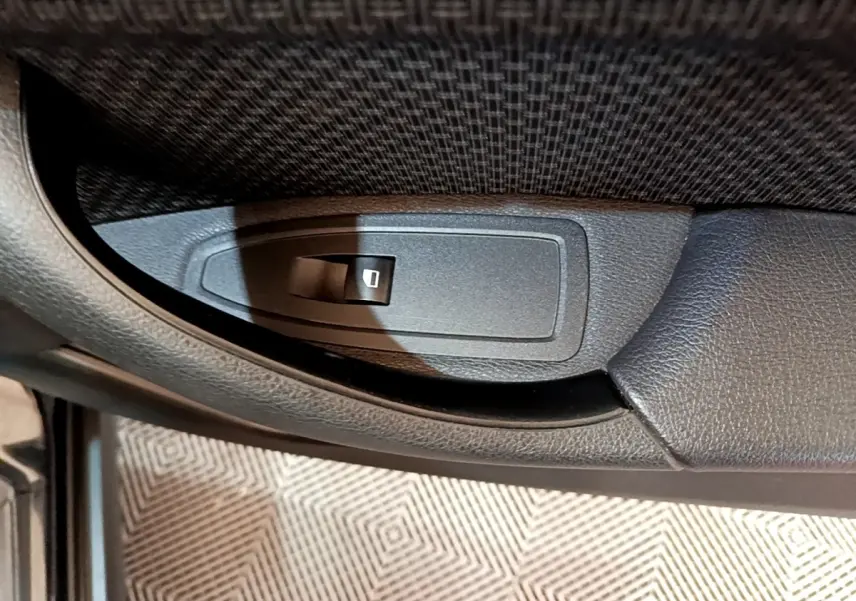 Gros plan sur le bouton de commande de lève-vitre côté gauche intérieur d'une BMW X2 sDrive18i Lounge noire 2023.