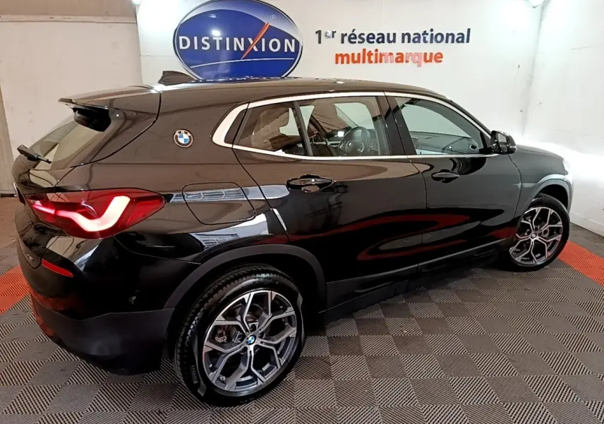 Vue 3/4 arrière droite d’un BMW X2 sDrive18i Lounge noir brillant avec jantes alliage et feux arrière LED allumés.