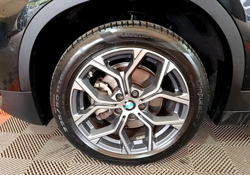 Gros plan sur la roue avant gauche noire d’un BMW X2 sDrive18i Lounge avec jante alliage gris et logo BMW central.