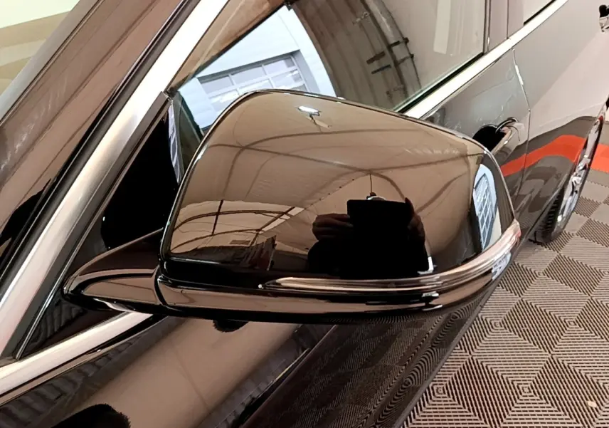 Gros plan sur le rétroviseur côté gauche noir brillant d’une BMW X2 sDrive18i Lounge 2023 avec reflet de l’environnement intérieur.