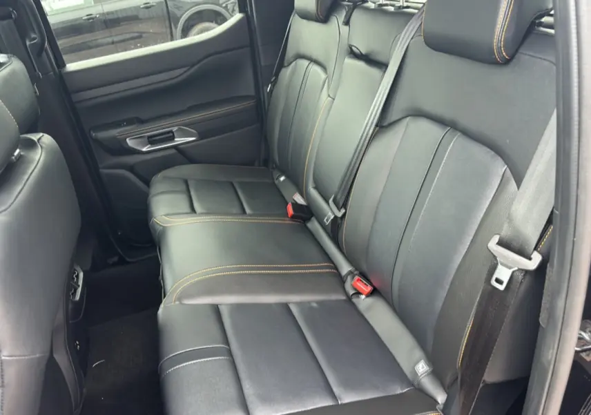 Vue intérieure côté arrière droit du Ford Ranger 3.0 V6 Wildtrak Plus, sièges cuir noirs avec surpiqûres orange.