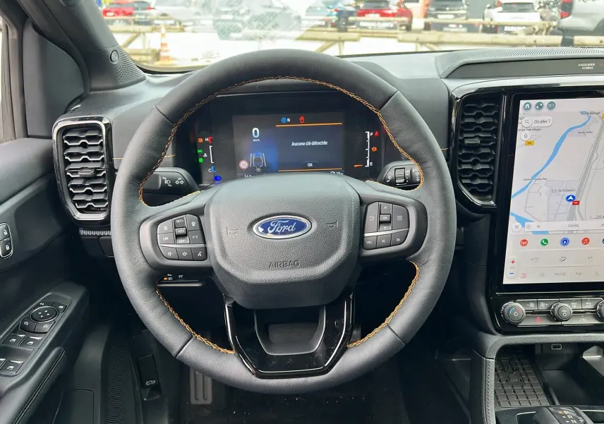 Vue intérieure frontale du volant cuir noir avec coutures orange du Ford Ranger 2026, écran digital et écran tactile GPS à droite.