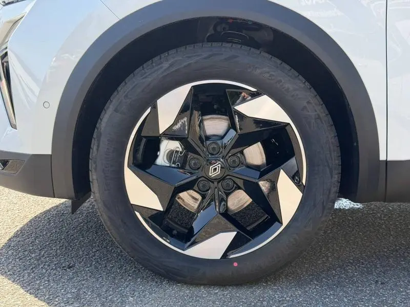 Gros plan sur la roue avant droite du Renault Captur blanc nacré, avec jante alu noire et argent au design géométrique.