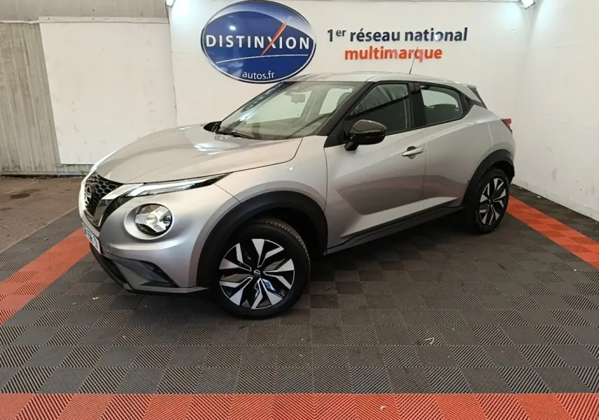 Nissan Juke gris clair en 3/4 avant droit, avec jantes noires et grises, dans un showroom intérieur.