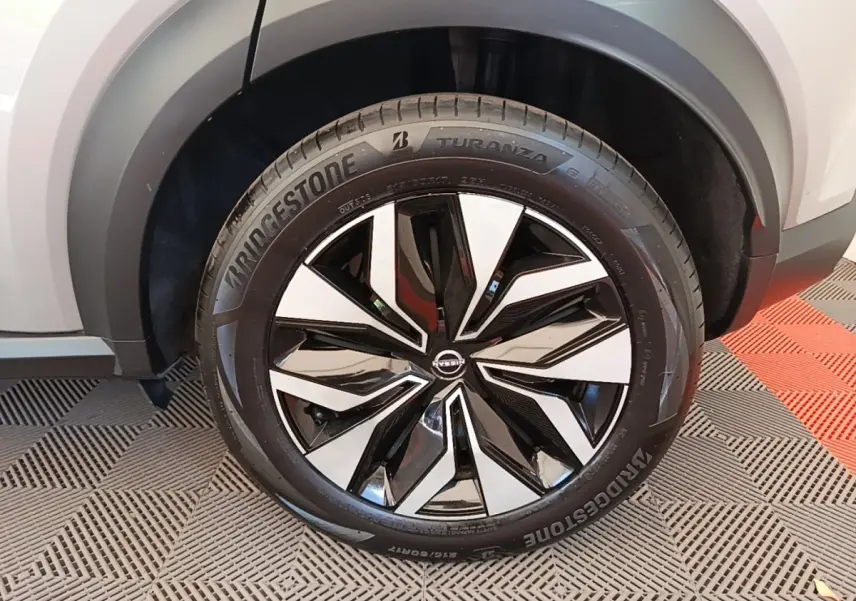 Gros plan sur la roue avant droite du Nissan Juke gris clair 2023 avec jante alliage bicolore et pneu Bridgestone.