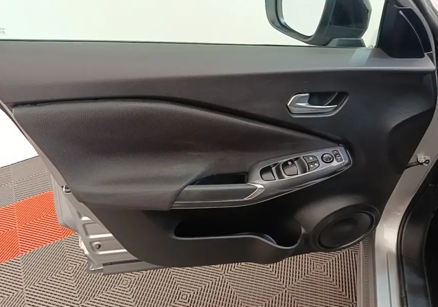 Vue intérieure de la porte avant gauche gris clair du Nissan Juke 2023 avec commandes électriques et haut-parleur intégré.
