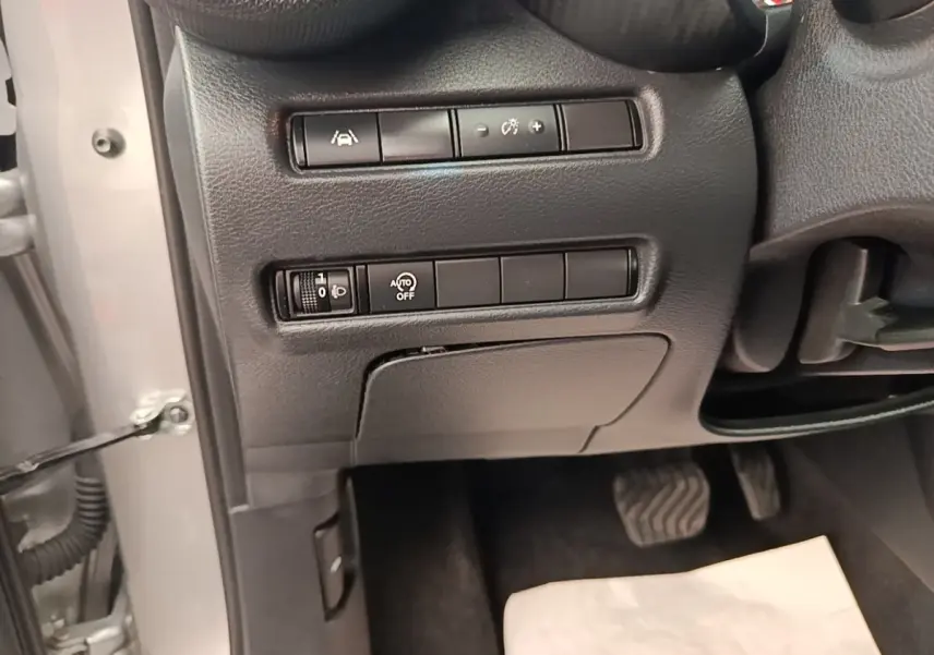 Détail du tableau de bord côté gauche avec commandes d'assistance et réglage des phares sur Nissan Juke gris clair 2023.