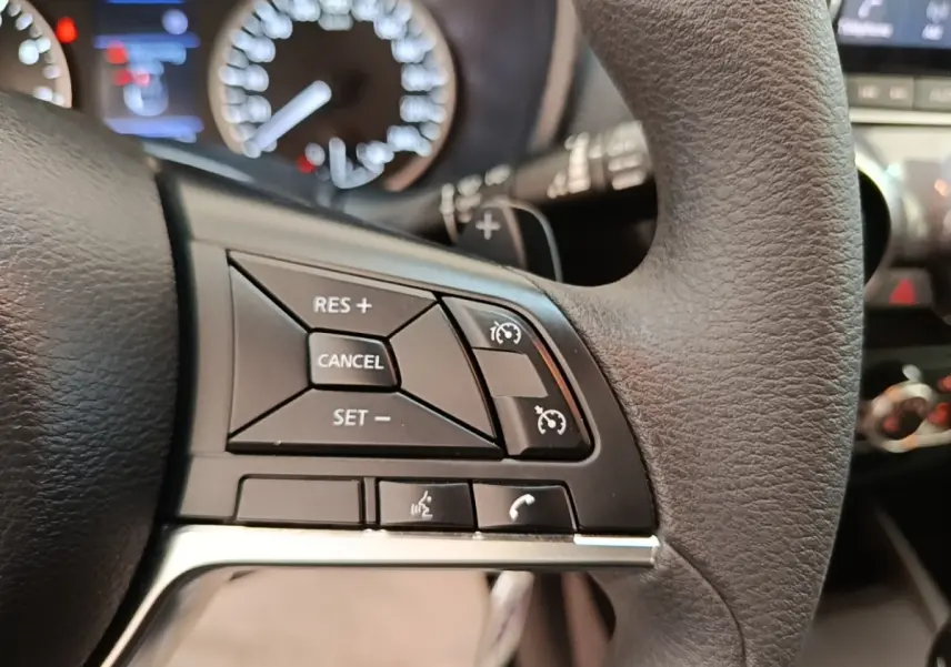 Gros plan sur les commandes du régulateur de vitesse au volant noir du Nissan Juke 2023, tableau de bord flou en arrière-plan.