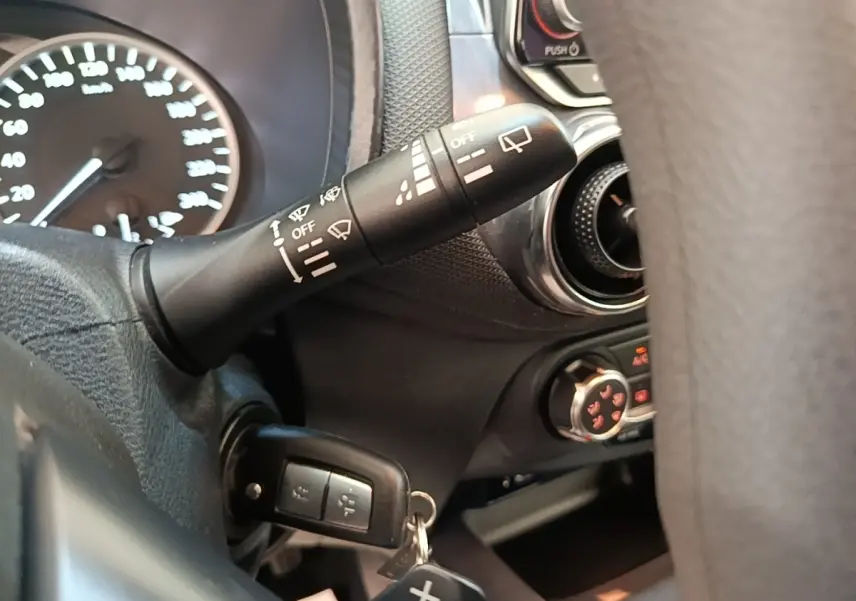 Gros plan intérieur sur la commande d’essuie-glace et le tableau de bord noir du Nissan Juke gris clair 2023.