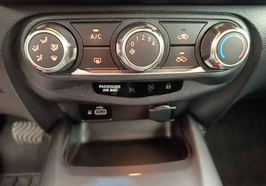 Détail du tableau de bord du Nissan Juke 2023 avec commandes climatisation, ports USB et prise 12V visibles.
