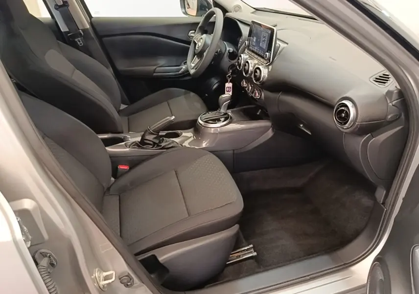 Intérieur avant droit du Nissan Juke gris clair 2023, montrant sièges tissu noirs et tableau de bord avec écran tactile.