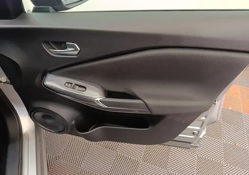 Vue rapprochée de la porte avant gauche gris clair du Nissan Juke 2023 avec commandes de vitres et haut-parleur intégré.