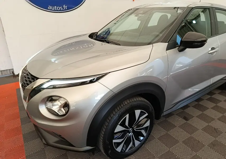Nissan Juke gris clair en 3/4 avant droit, avec phares LED et jantes alliage bicolores visibles.