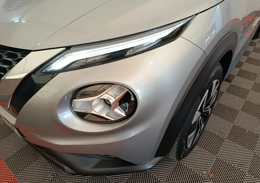 Gros plan sur l'avant droit gris clair du Nissan Juke 2023, mettant en valeur son phare LED et la jante stylisée.