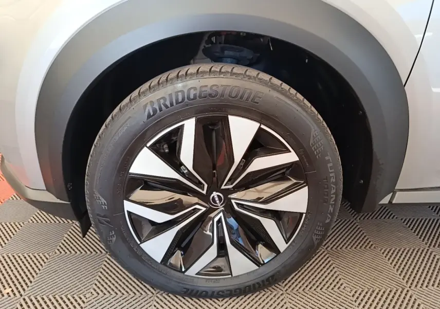 Gros plan sur la roue avant droite du Nissan Juke gris clair, jante alliage noir et argent au design moderne.