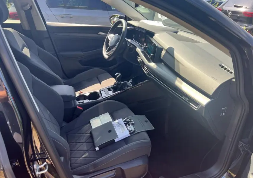 Vue intérieure côté conducteur de la Volkswagen Golf VIII noire, montrant sièges en microfleece et tableau de bord moderne.