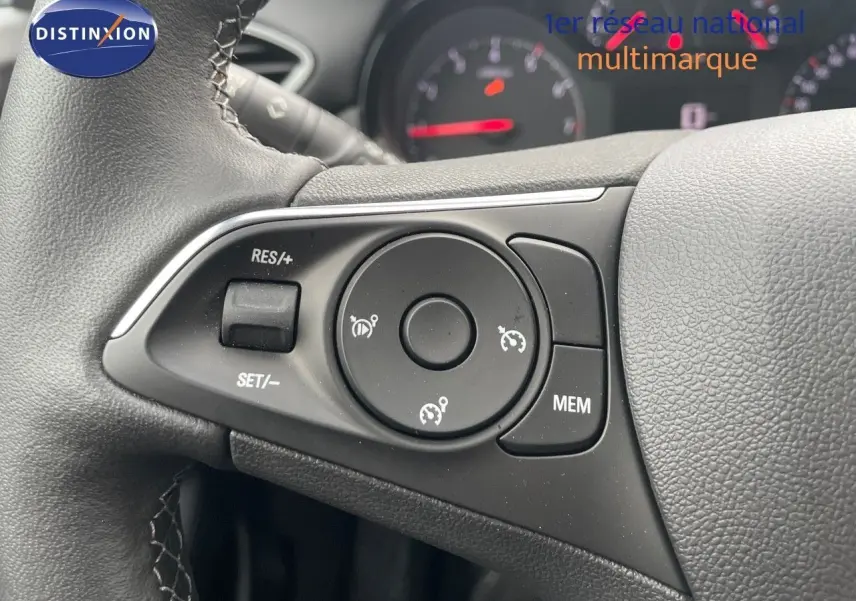 Gros plan sur les commandes au volant du Opel Crossland gris minéral 2022, avec tableau de bord flou en arrière-plan.