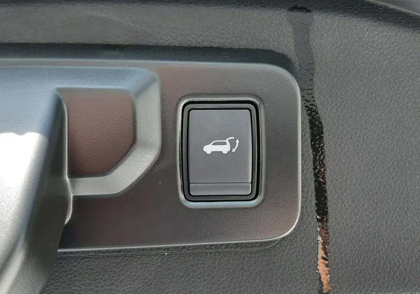 Bouton noir de commande d'ouverture du coffre sur la garniture intérieure d'un Renault Espace VI gris schiste métal.