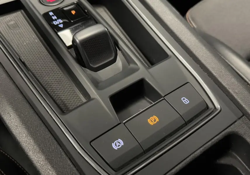 Gros plan sur la console centrale noire de la CUPRA Leon Sportstourer 1.4 e-Hybrid avec levier de vitesse et boutons éclairés.